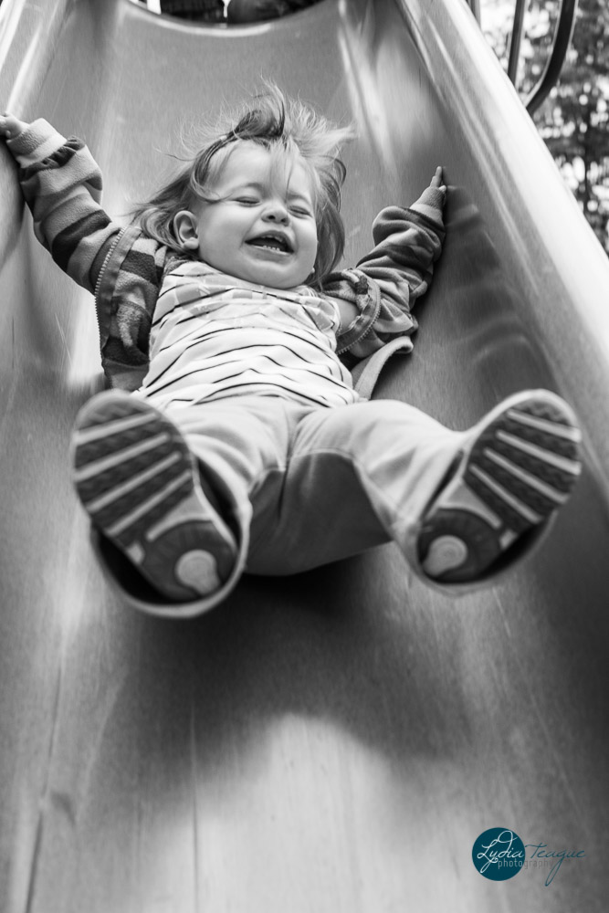 Toddler flying down the slide. Black and white photo taken by Dripping Springs TX based Lydia Teague Photography. 