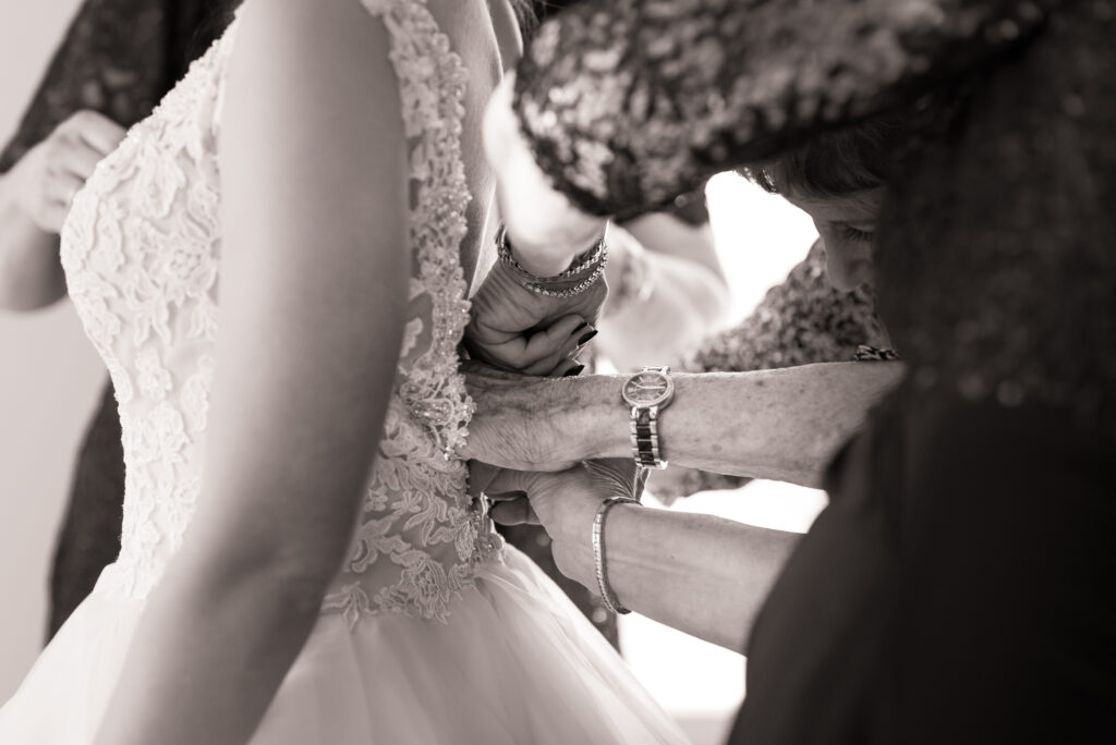 Ladies hands working to zip up the bride in her dress. black and white, texture. Photo taken by Dripping Springs TX based Lydia Teague Photography. 