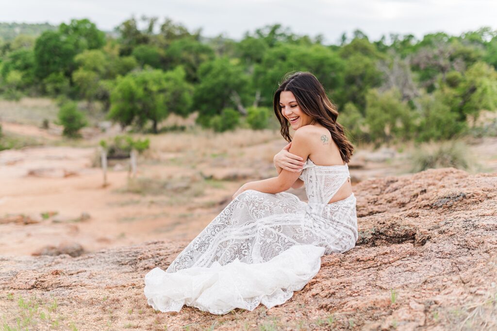 Dark haired Bride sitting on pink granite rock in a white wedding dress. Dripping Springs Wedding Photographer Lydia Teague Photography.