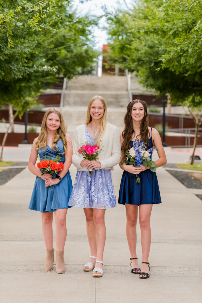 Freshman girls wearing blue dresses holding bouquets for the homecoming dance.
