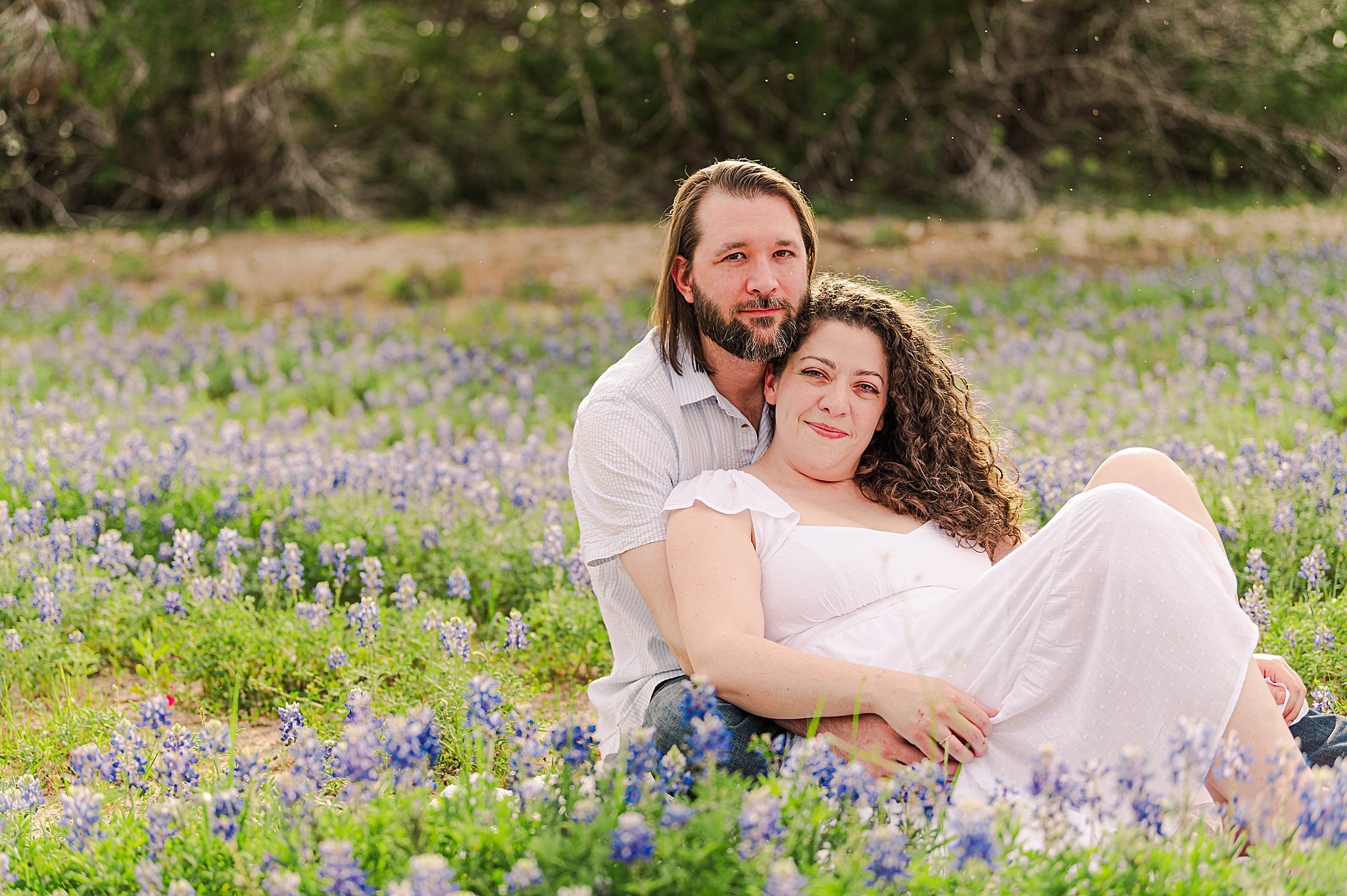 An Engaged Couple comfortably embraces in a field of bluebonnets. Dripping Springs Engagement Photographer Lydia Teague