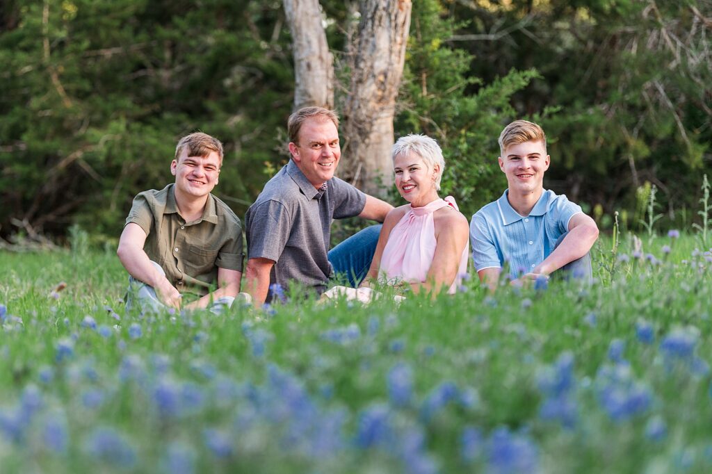 A Family of 4 sitting in the bluebonnets and smiling.
