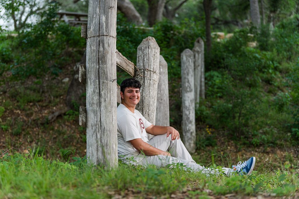 A high school senior boy sitting with his legs straight in front of him and leaning back on an old white fence. What to bring to my senior portraits?
