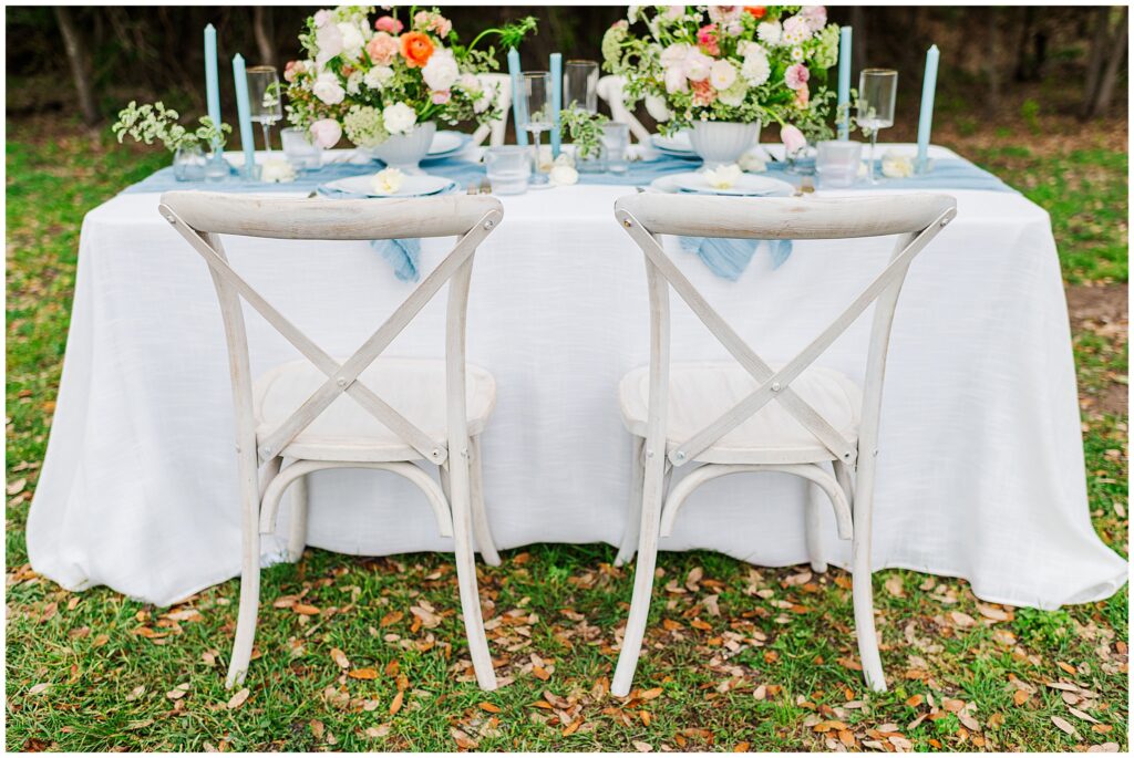 Criss cross backed reception chairs with a whimsical floral themed tablescape in pastel orange, peach, and pink flowers. With a pop of Something Blue linens. Photo taken by Dripping Springs TX based Lydia Teague Photography. 