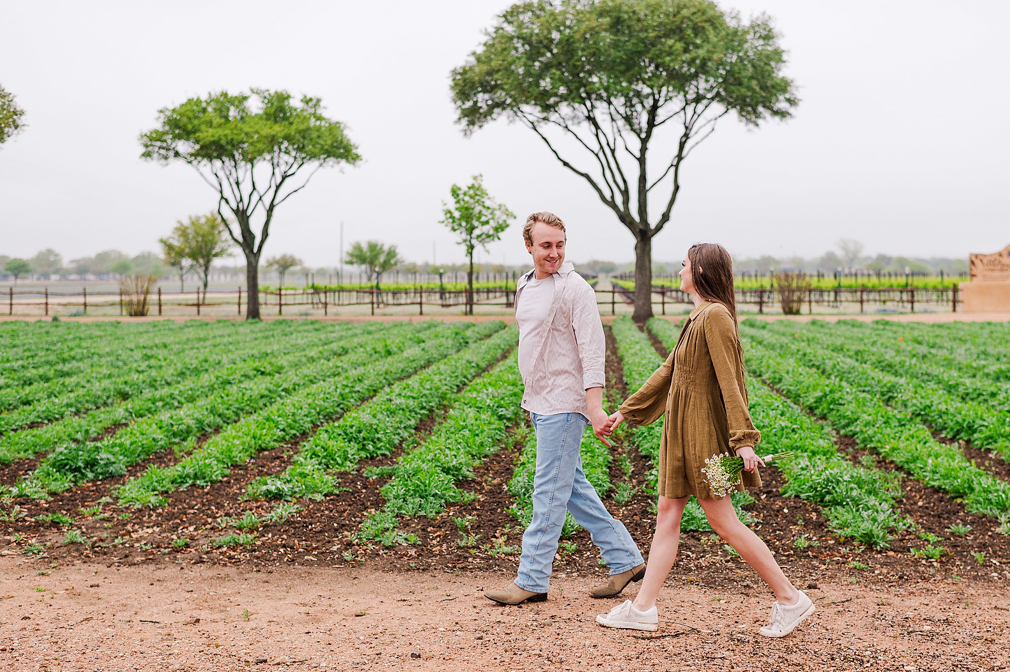 A young couple walking beside rows of planted flowers. Photo taken by Dripping Springs TX based Lydia Teague Photography.